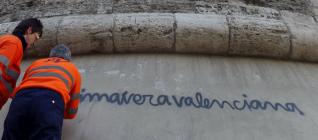 Unos operarios limpian una pintada con el lema "Primavera valenciana" en las torres de Quart.