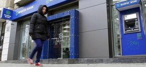 Una mujer camina junto un banco chipriota.