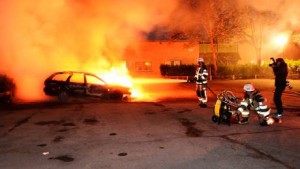Un grupo de bomberos trata de extinguir un vehículo en llamas tras los disturbios registrados en el barrio de Kista, en Estocolmo, Suecia