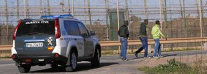Tres inmigrantes pasean junto a la frontera de Melilla ante la atenta mirada de una patrulla de la Guardia Civil  