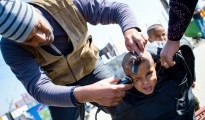 Un niño gesticula mientras le cortan el pelo en el campamento donde vive junto a multitud de migrantes y refugiados en Idomeni, en la frontera greco-macedonia, el 19 de marzo de 2016
