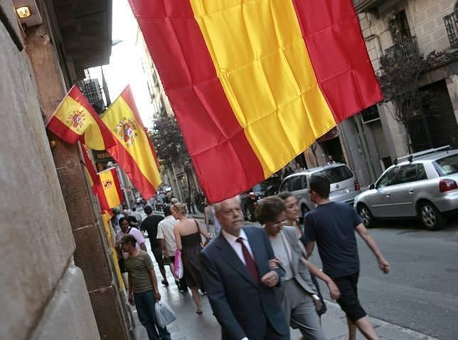 Transeúntes pasean por una calle de Barcelona con banderas españolas