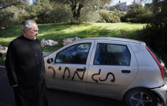 El abad ortodoxo griego del Monasterio de la Santa Cruz en Jerusalén, el archimandrita Claudio, mira un coche rociado con un graffitti anti-cristianos que dice. "precio" y con los neumáticos desinflados a las afueras de su monasterio.