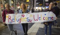 Tres jóvenes suecas muestran una pancarta muestra una pancarta dando la bienvenida a los refugiados