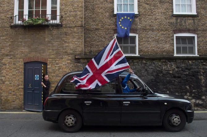 Un taxista londinense ondea una bandera británica mientras circula por una calle donde una bandera europea ondea en una ventana en Londres (Reino Unido) hoy, 24 de junio de 2016.