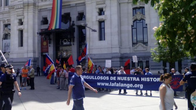Imagen de algunos manifestantes junto la pancarta con el lema: "Orgullosos de nuestra historia". Al fondo, colgada en el Ayuntamiento, la bandera del arcoiris gay.