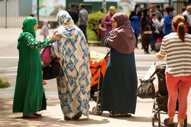 Mujeres ataviadas con velo esperan a sus hijos en la puerta de un colegio. 