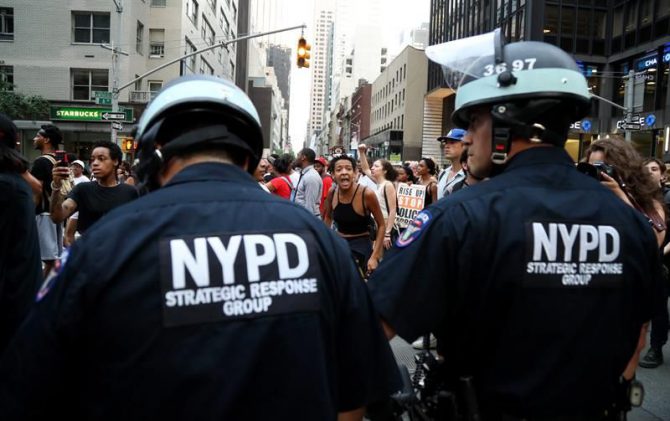 Un grupo de personas protestan frente a miembros del Grupo de Respuesta Estratégica de la Policía de Nueva York.
