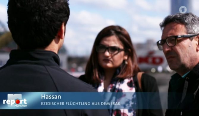Hasan (izquierda), un refugiado yazidí en Alemania que ha sido amenazado por musulmanes, cuenta a un reportero de la televisión estatal germana cómo el traductor a sueldo del Estado tradujo mal deliberadamente su denuncia y se puso de parte de los atacantes. (Imagen: captura de un vídeo de Bayerischer Rundfunk)