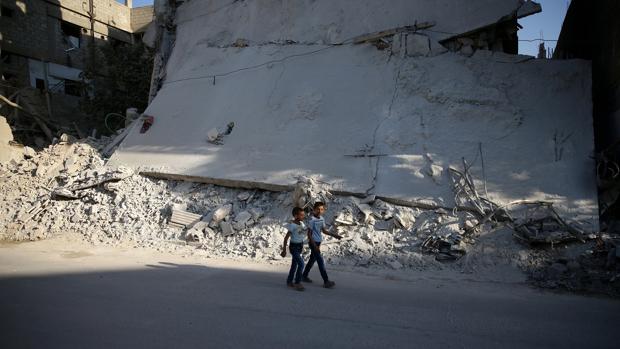 Dos niños caminan junto a un edificio bombardeado en un barrio rebelde de Damasco
