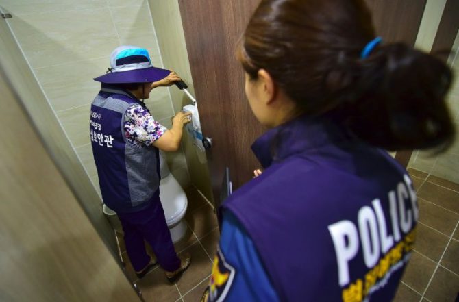 Una integrante del equipo de "caza de cámaras ocultas" de Seúl (i) y una agente de policía inspeccionan un baño de mujeres en un museo de la ciudad el 18 de agosto de 2016