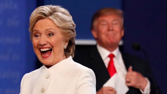 Hillary Clinton sonriendo a la audiencia, con Donald Trump situado al fondo, durante el tercer debate electoral