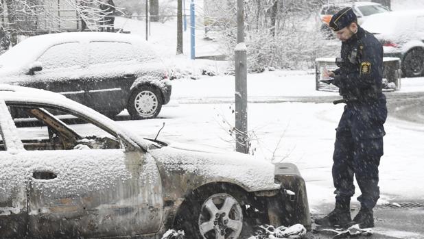 Un policía toma nota ante un vehículo calcinado durante unos disturbios en el suburbio de Rinkeby, este lunes en Estoc