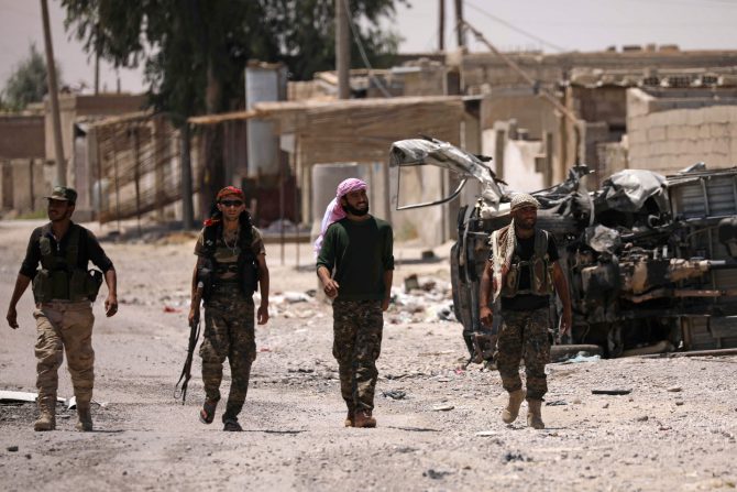 Varios hombres de las Fuerzas Democráticas Sirias caminan junto a un vehículo destruido en Raqa. 11 de junio de 2017. 