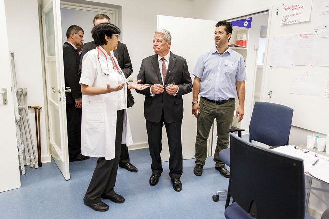 El presidente de Alemania, Joachim Gauck, conversa con un grupo de médicos en la enfermería de un centro de acogida de inmigrantes en Berlin-Wilmersdorf, el 26 de agosto de 2015. (Foto: Jesco Denzel/Bundesregierung vía Getty Images).