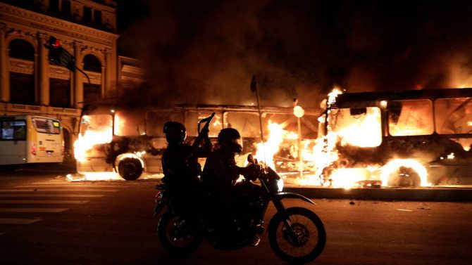 Policías antidisturbios pasan frente a unos autobuses en llamas en Rio de Janeiro
