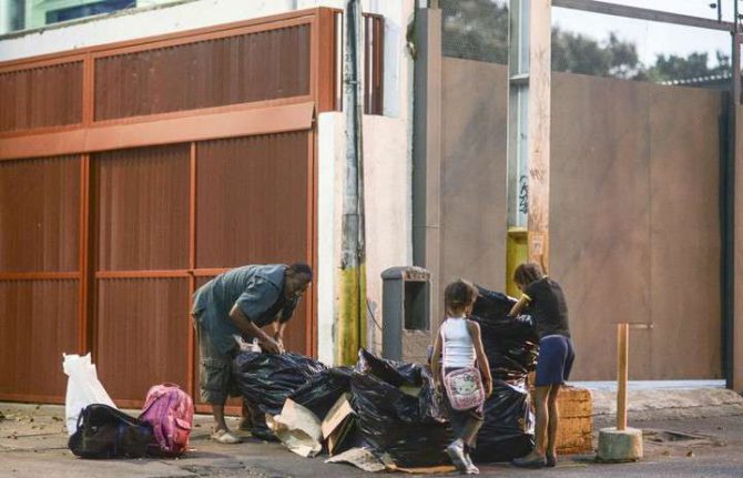 Un hombre junto a una niña busca comida en la basura en Caracas.