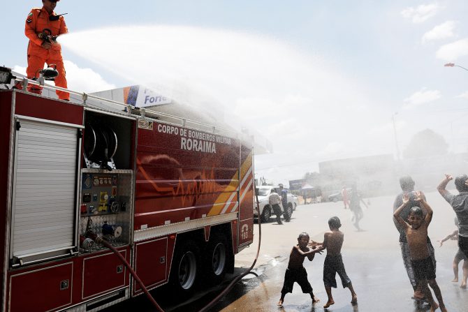 Bomberos brasileños mojan a niños venezolanos en Boa Vista, estado de Roraima