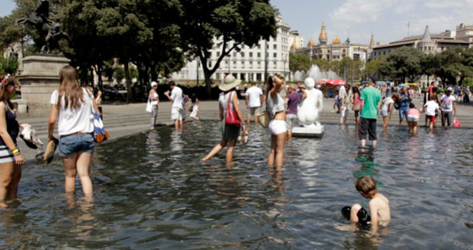 Unos turistas se bañan en la plaza Cataluña de Barcelona