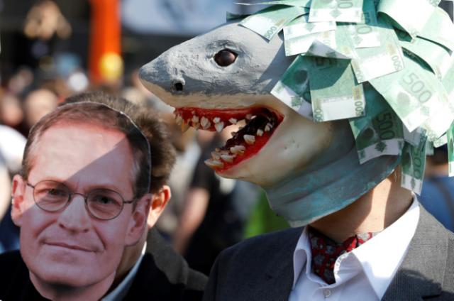Un manifestante exhibe una máscara de tiburón mientras que otro porta una máscara del alcalde de Berlín, Michael Mueller, en la protesta contra el encarecimiento de la vivienda en Berlín